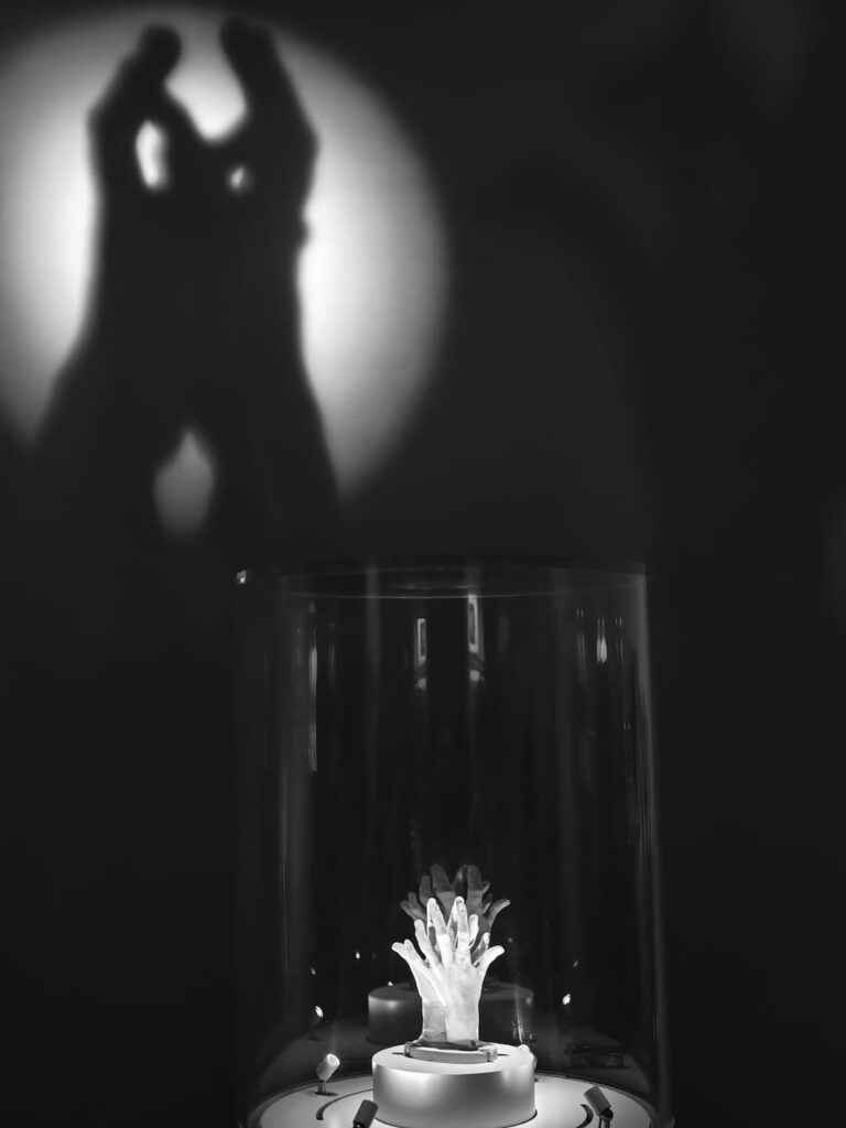 スマートフォンで撮影した手の彫刻と、それを斜め下からのライトアップで壁に影ができている